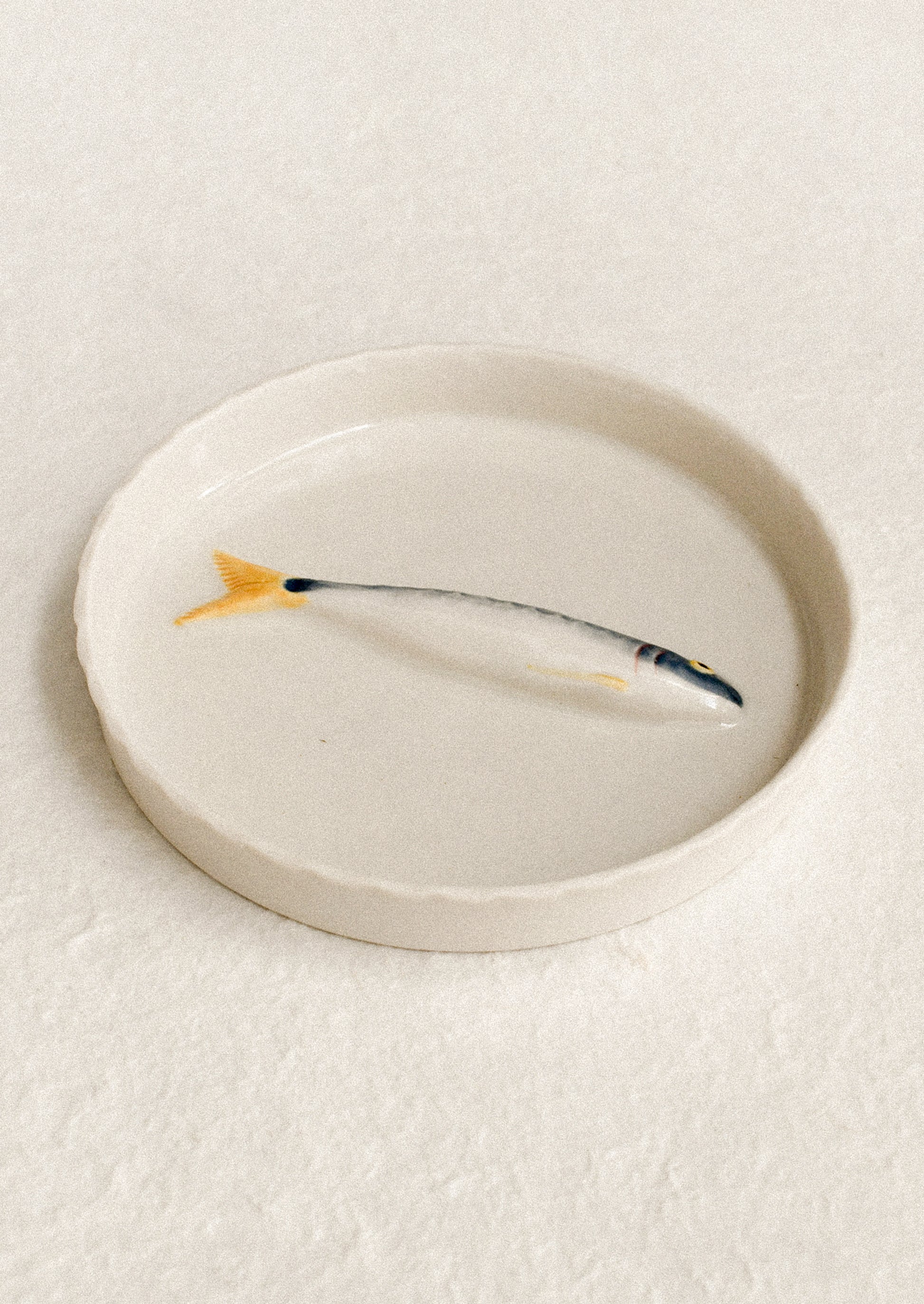 Ceramic fish-shaped object on a round plate with a plain background
