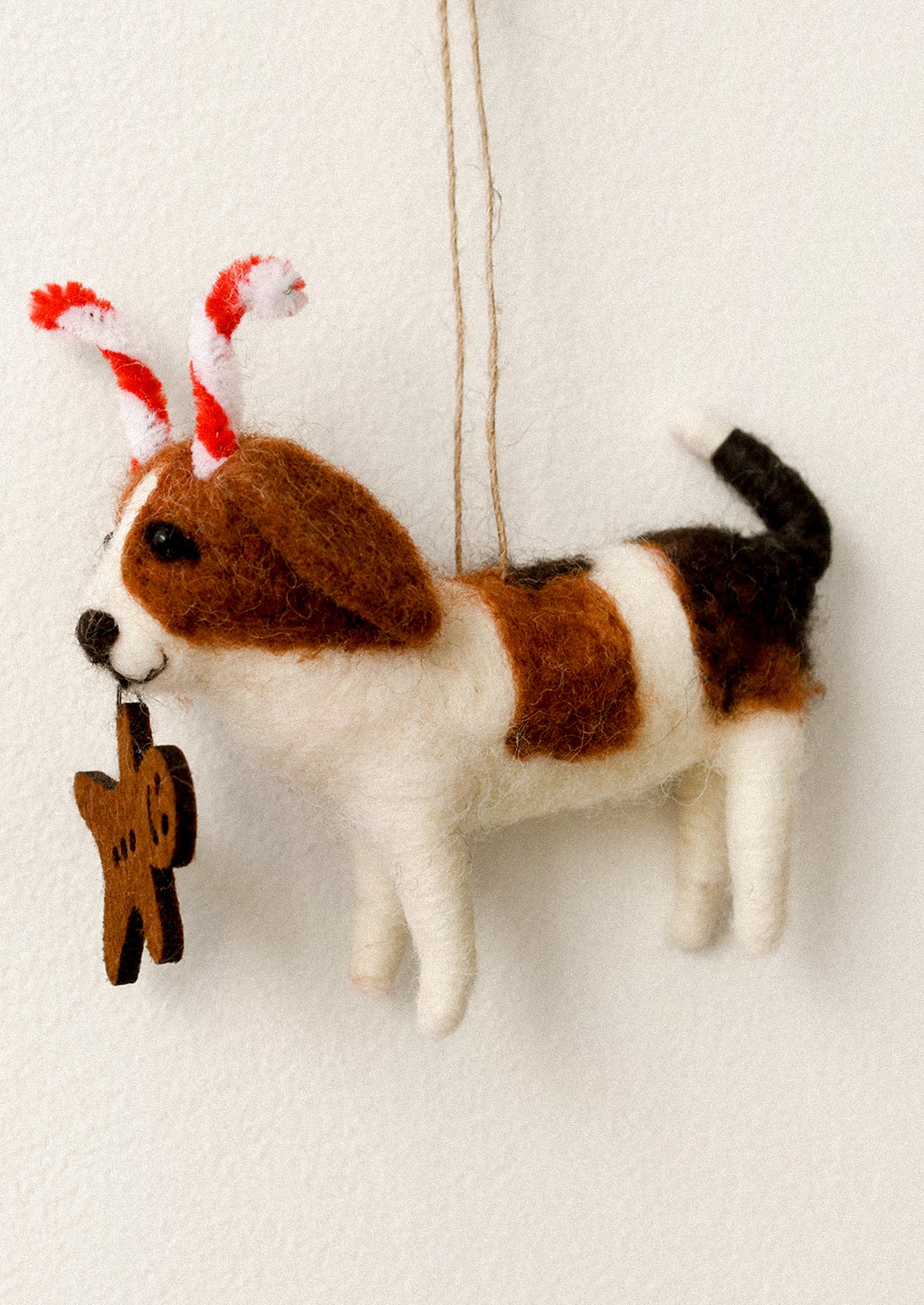 Felted dog ornament with candy cane ears and gingerbread cookie in mouth.