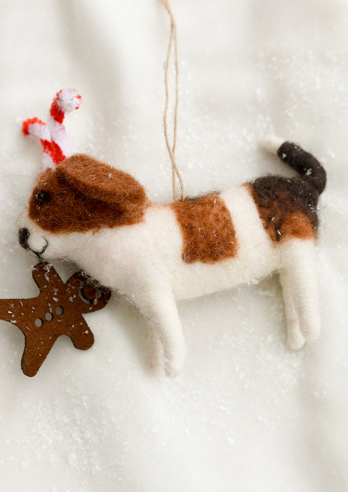 Felted dog ornament with candy cane ears and gingerbread cookie in mouth.