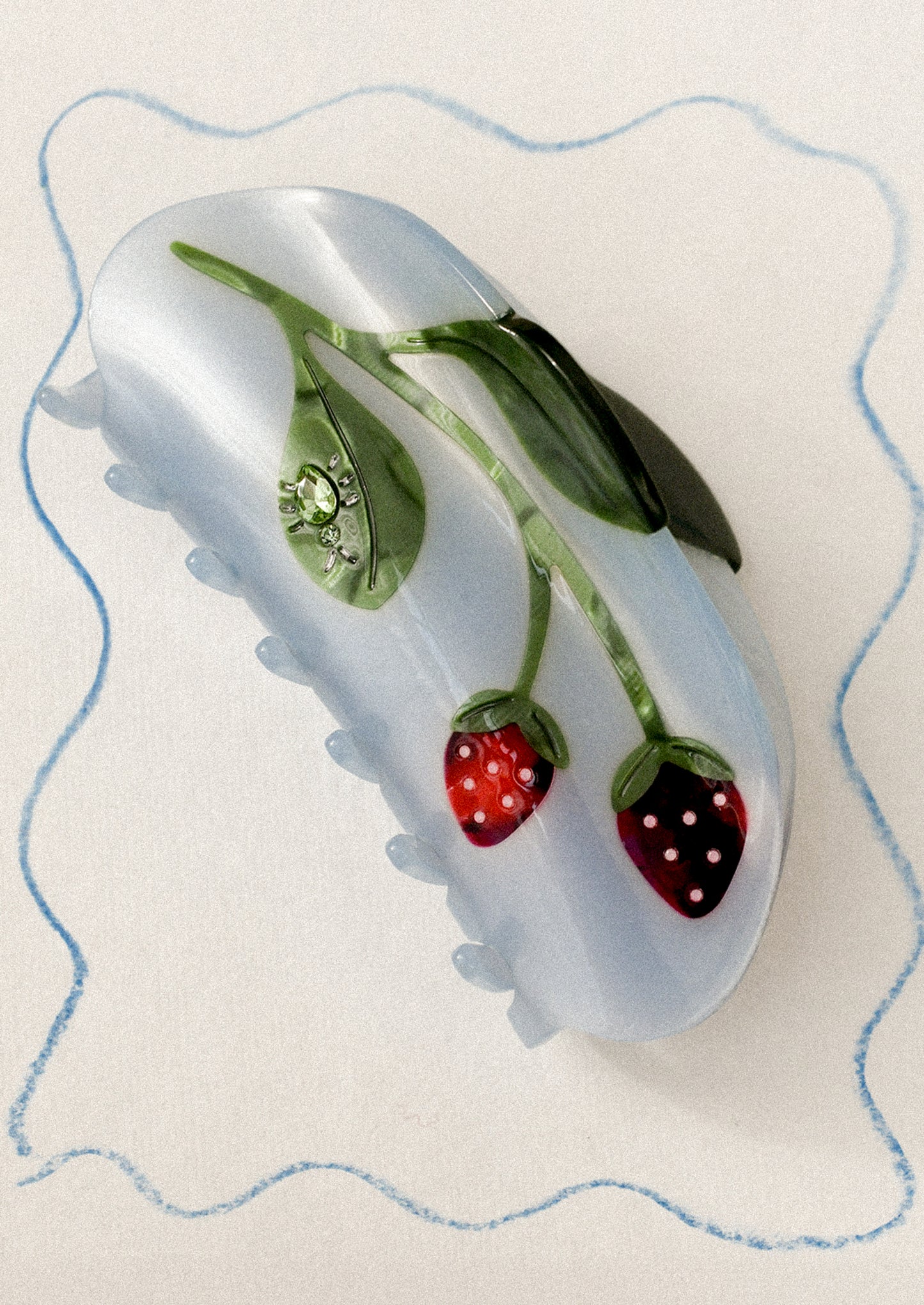 A blue hair claw with strawberry motif and jeweled bug on leaf.