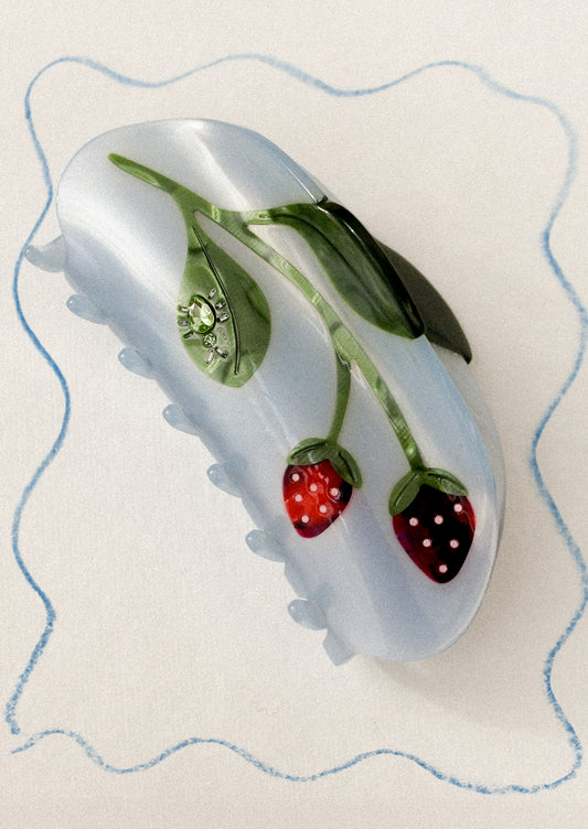 A blue hair claw with strawberry motif and jeweled bug on leaf.