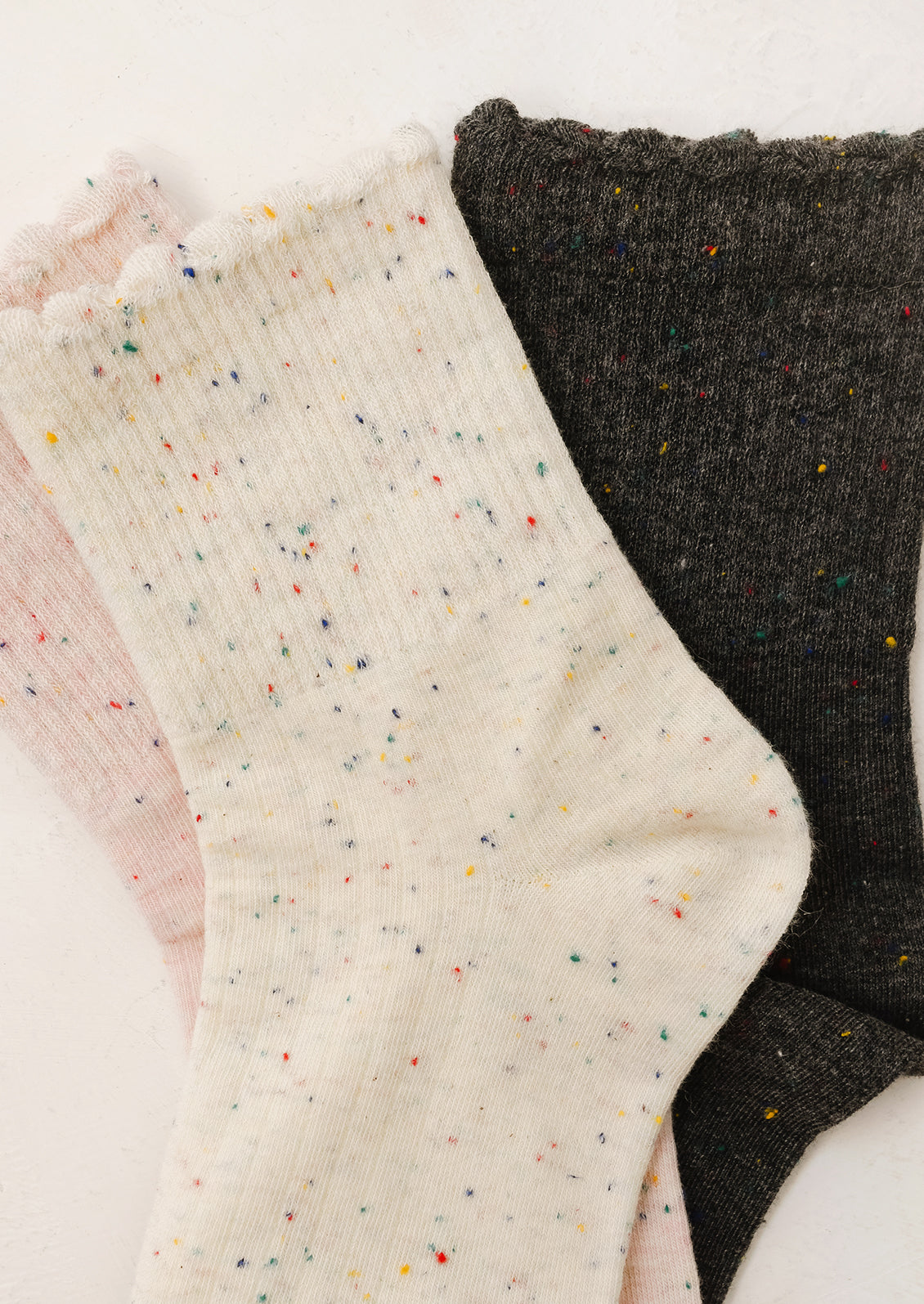 Three pairs of socks in pink, cream with speckles, and black on a light background