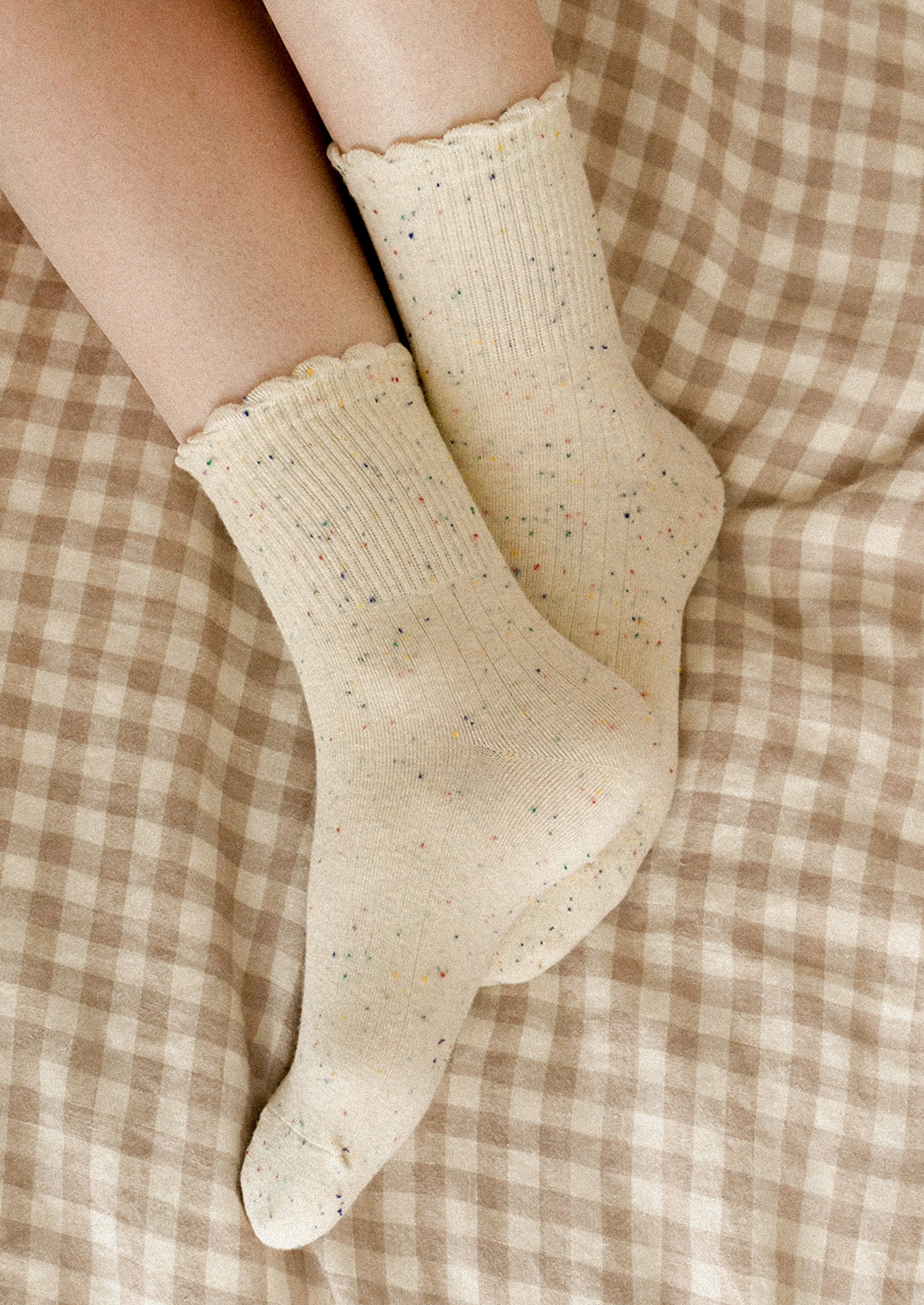 A person wearing a pair of cream socks with multicolor speckles.
