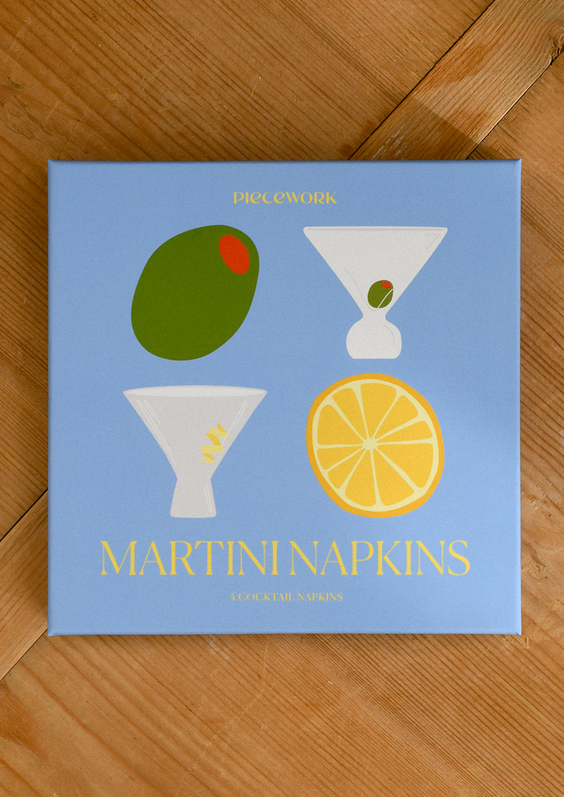 Pack of Martini Napkins with illustrations of an olive, a lemon, and a martini glass on a light blue background.