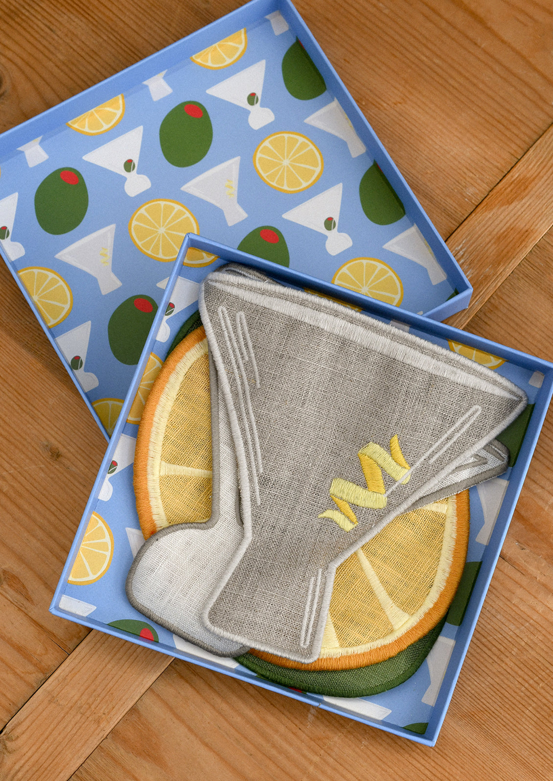 Set of decorative cocktail napkins shaped like an olive, lemon, and martini glass on a wooden surface.