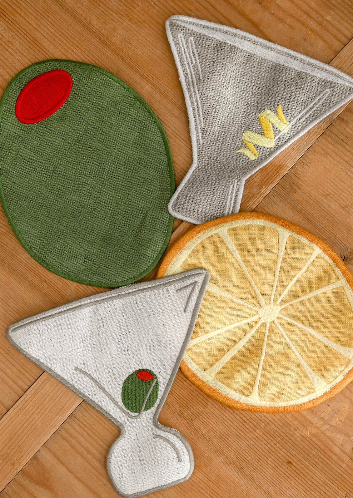 Set of decorative cocktail napkins shaped like an olive, lemon, and martini glass on a wooden surface.