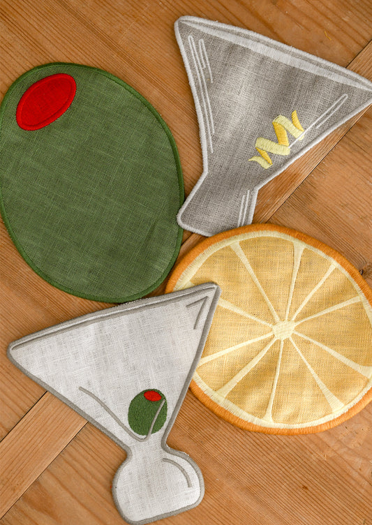 Set of decorative cocktail napkins shaped like an olive, lemon, and martini glass on a wooden surface.