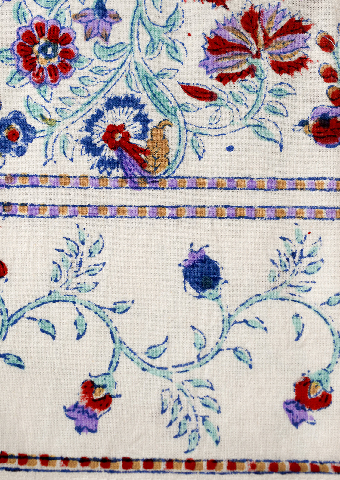Set of floral-patterned napkins in white with red, lavender and aqua color scheme on a wooden surface.