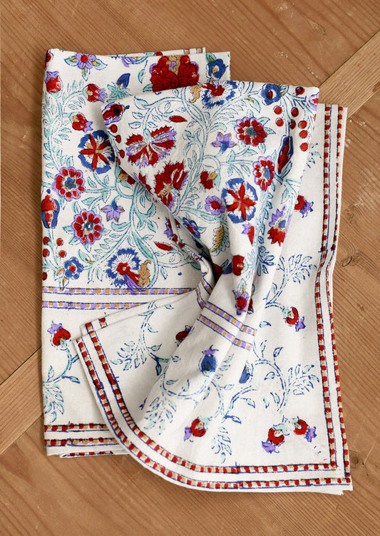 Set of floral-patterned napkins in white with red, lavender and aqua color scheme on a wooden surface.