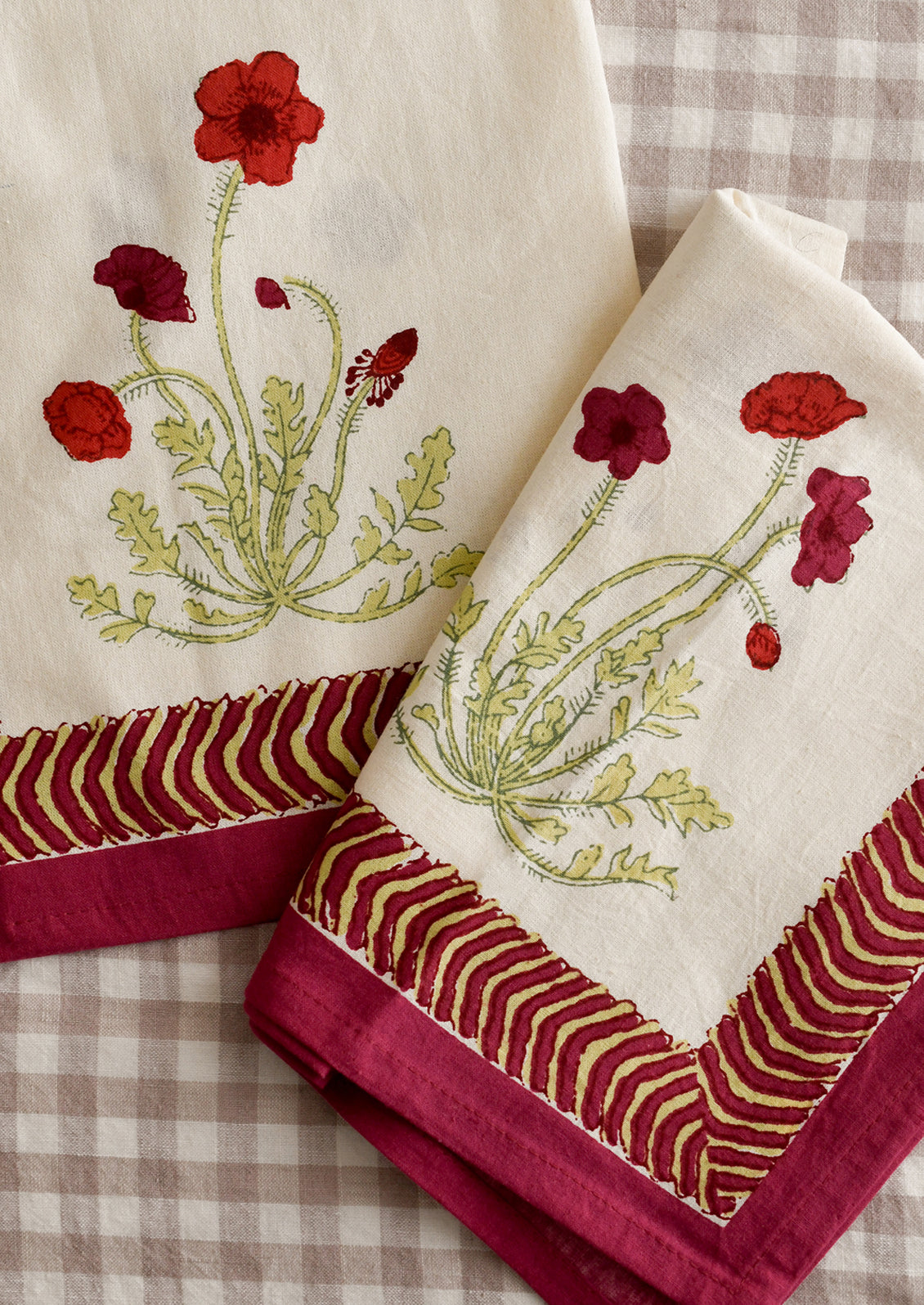 A pair of napkins with red poppy print and geometric red and green border.