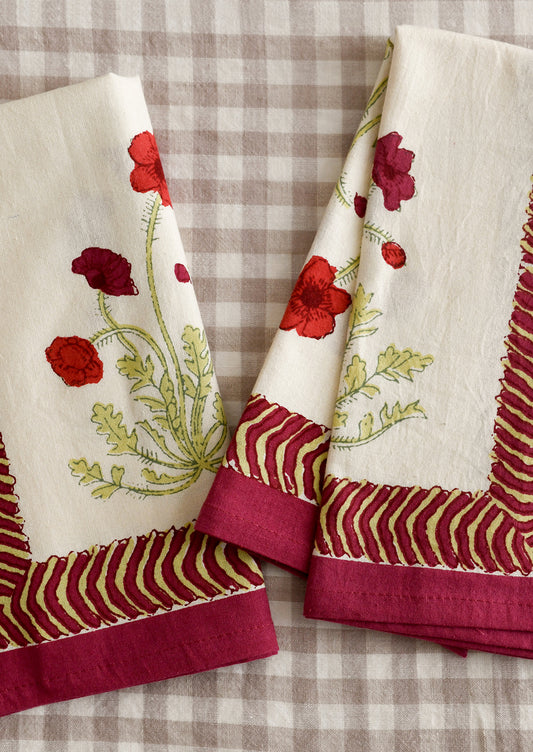A pair of napkins with red poppy print and geometric red and green border.