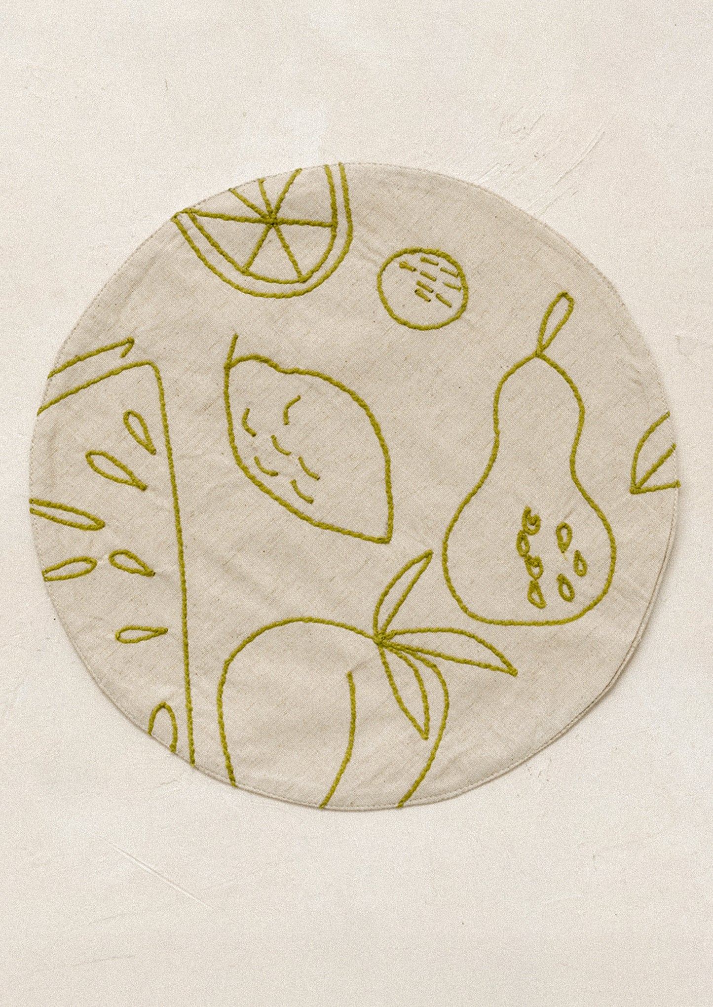 Round placemat with embroidered fruit design in green.