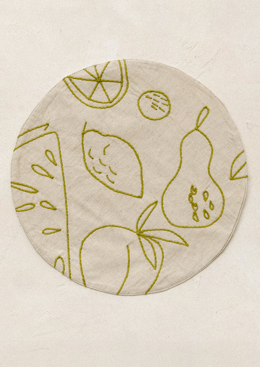 Round placemat with embroidered fruit design in green.