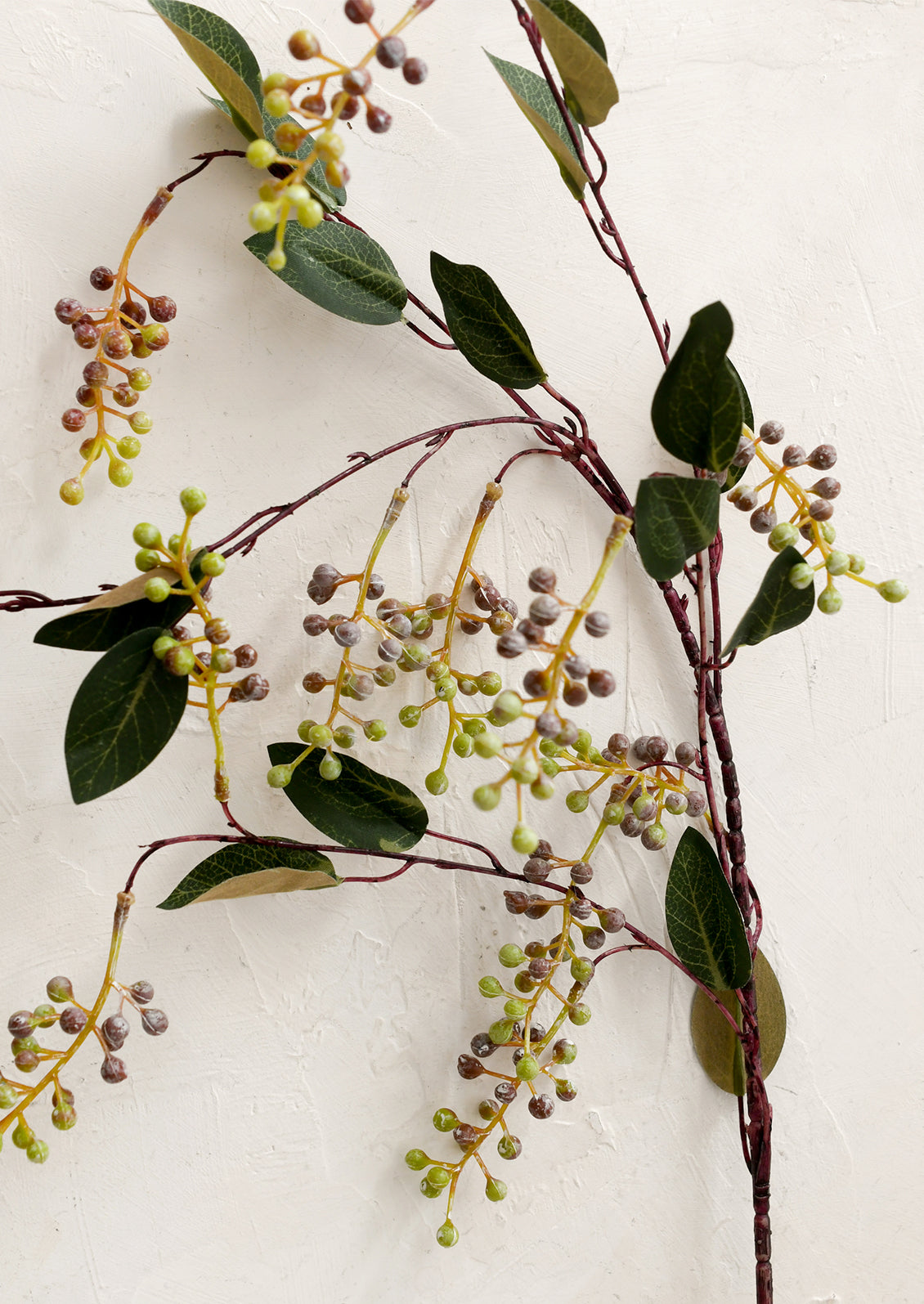 Artificial berry branch with green leaves and small berries on a white background
