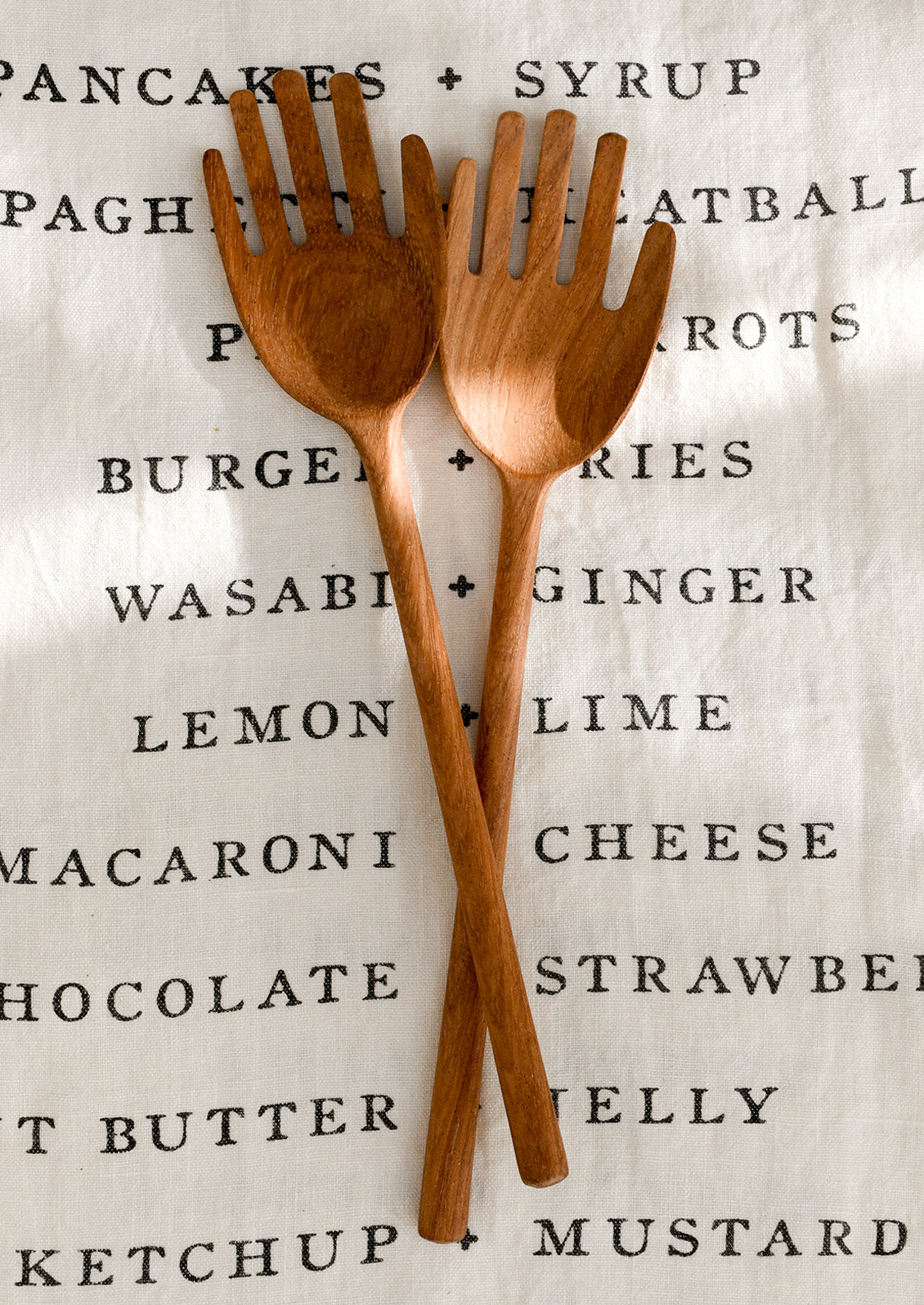 Two wooden salad servers shaped like hands on a light background