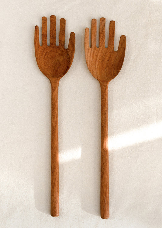 Two wooden salad servers shaped like hands on a light background