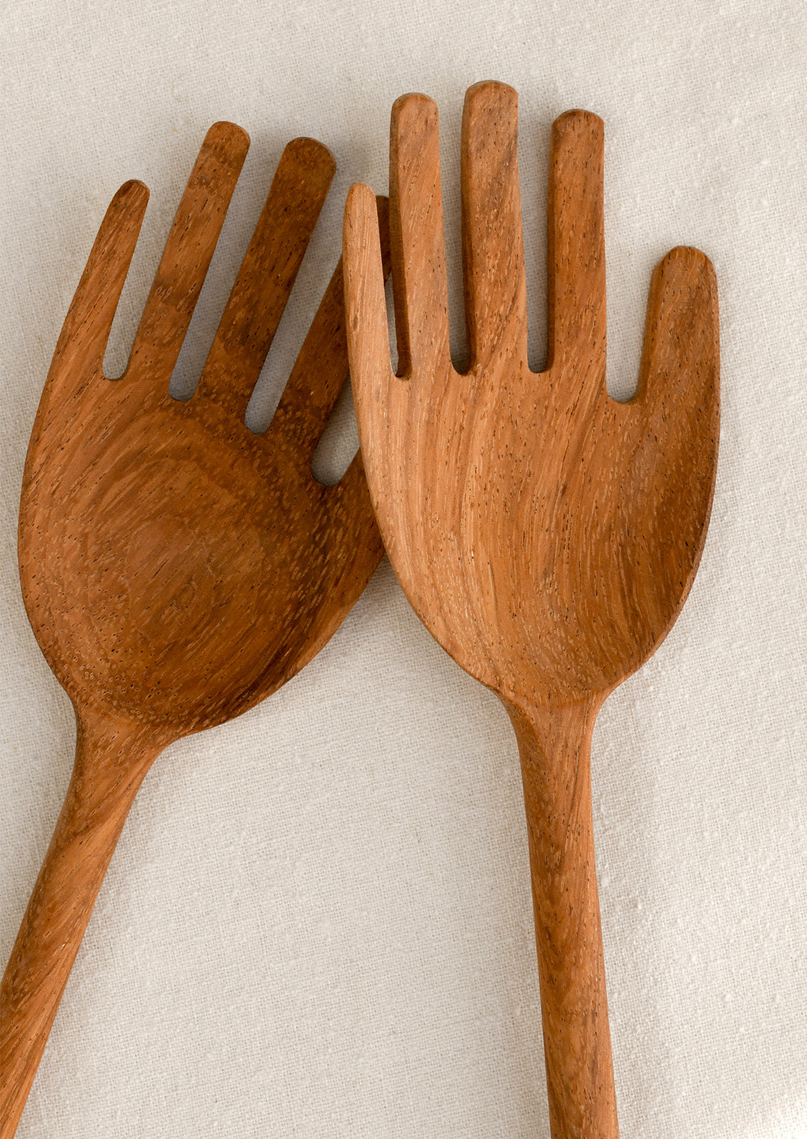 Two wooden salad servers shaped like hands on a light background