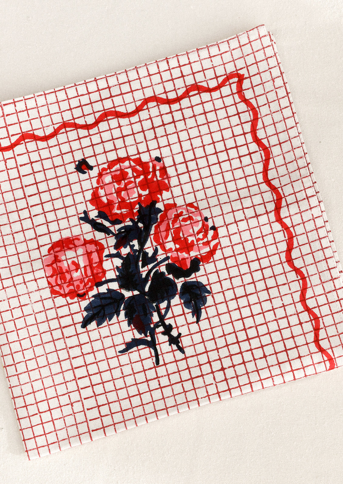 Red grid patterned cloth napkin with floral design and squiggle border.