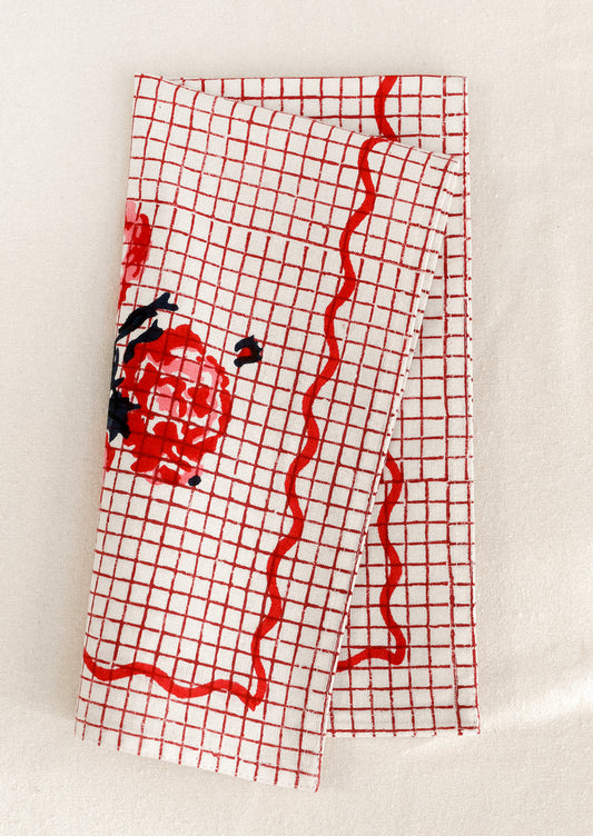 Red grid patterned cloth napkin with floral design and squiggle border.