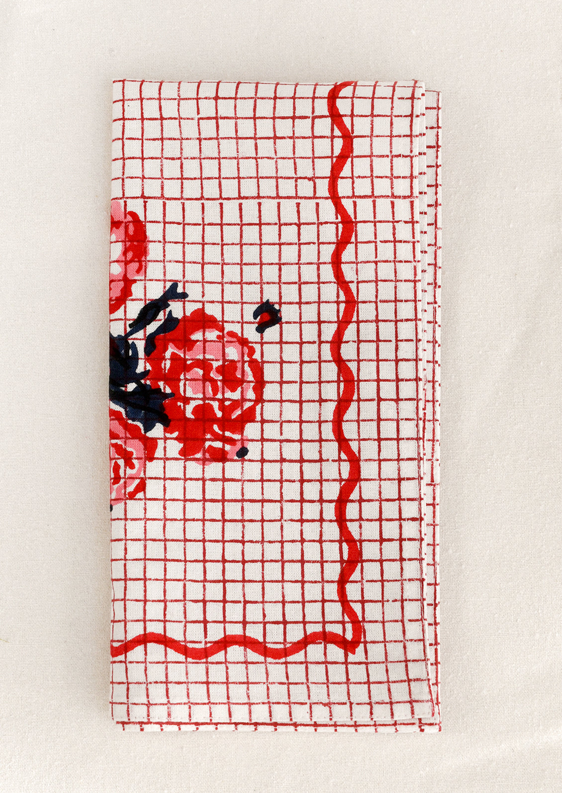 Red grid patterned cloth napkin with floral design and squiggle border.