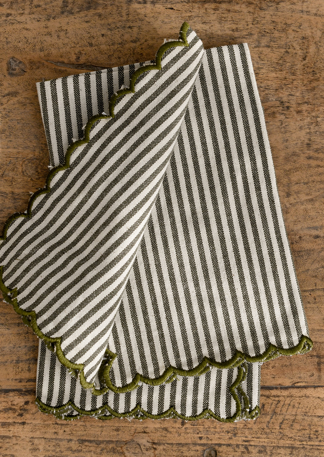 Striped napkin pair with green scalloped edge on a wooden surface