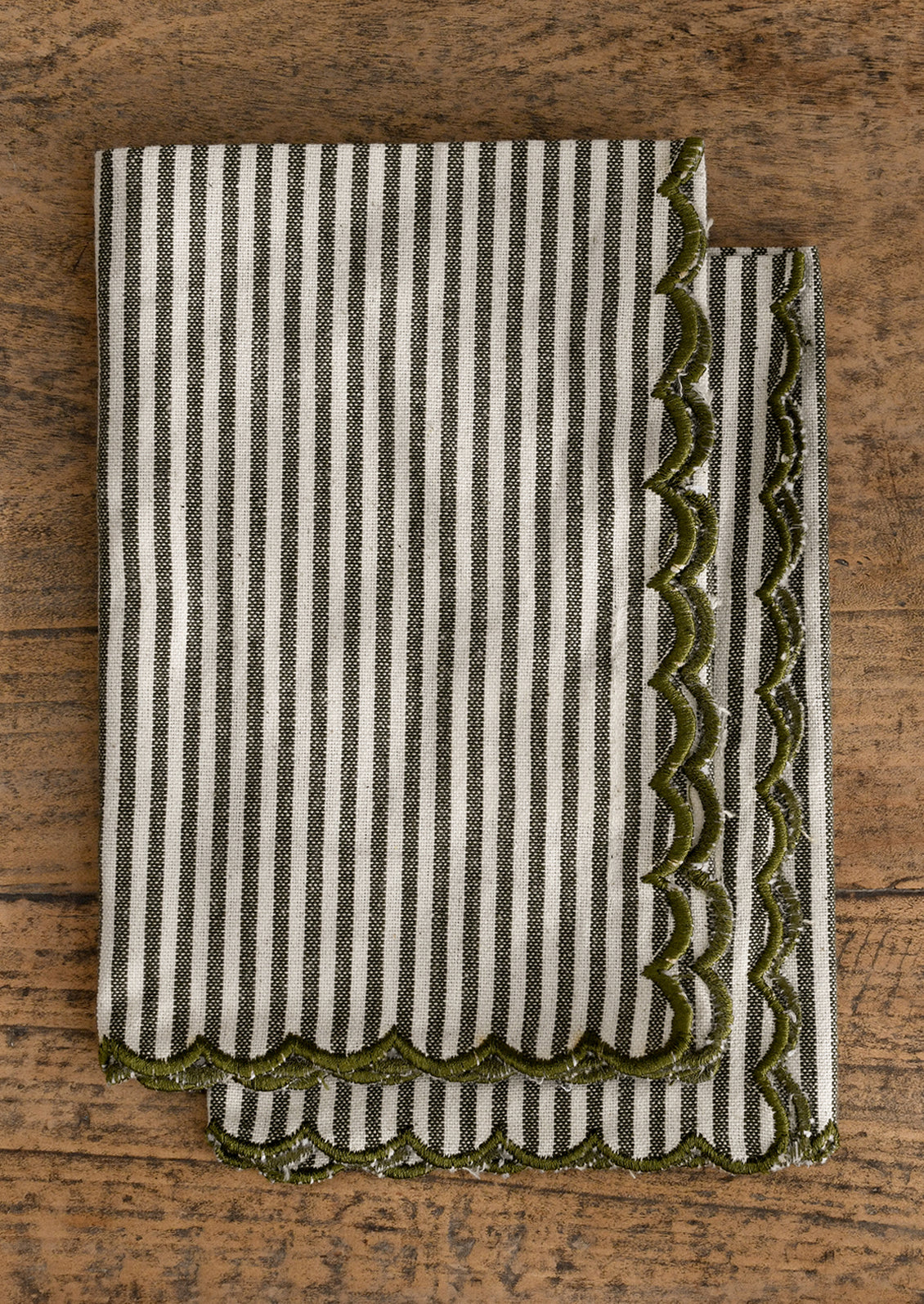 Striped napkin pair with green scalloped edge on a wooden surface