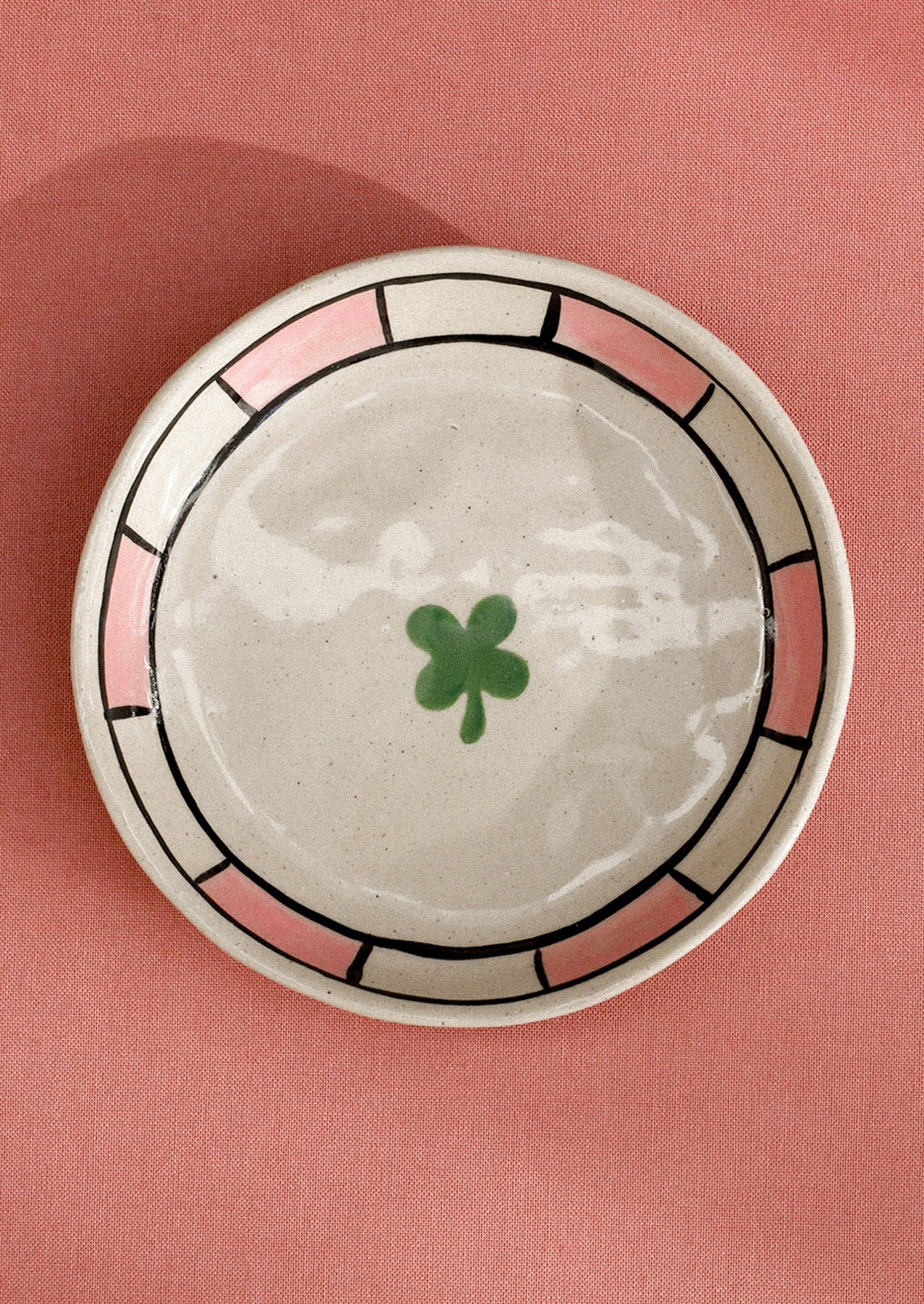 A small ceramic dish with raised sides with hand painted clover motif.