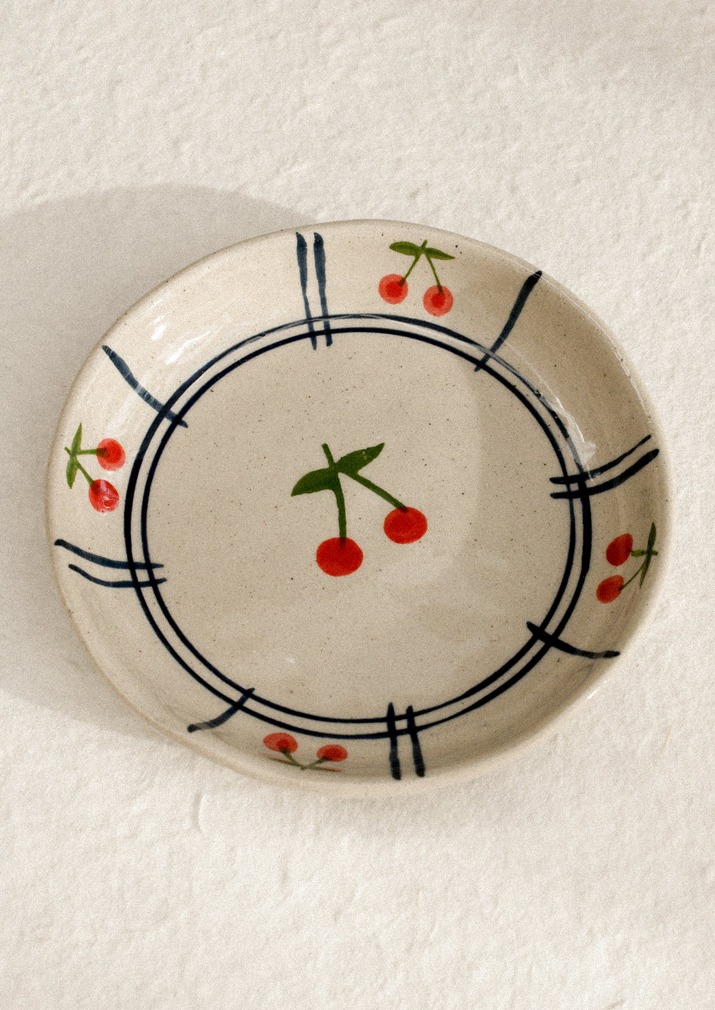 A small ceramic dish with raised sides with hand painted cherry motif.