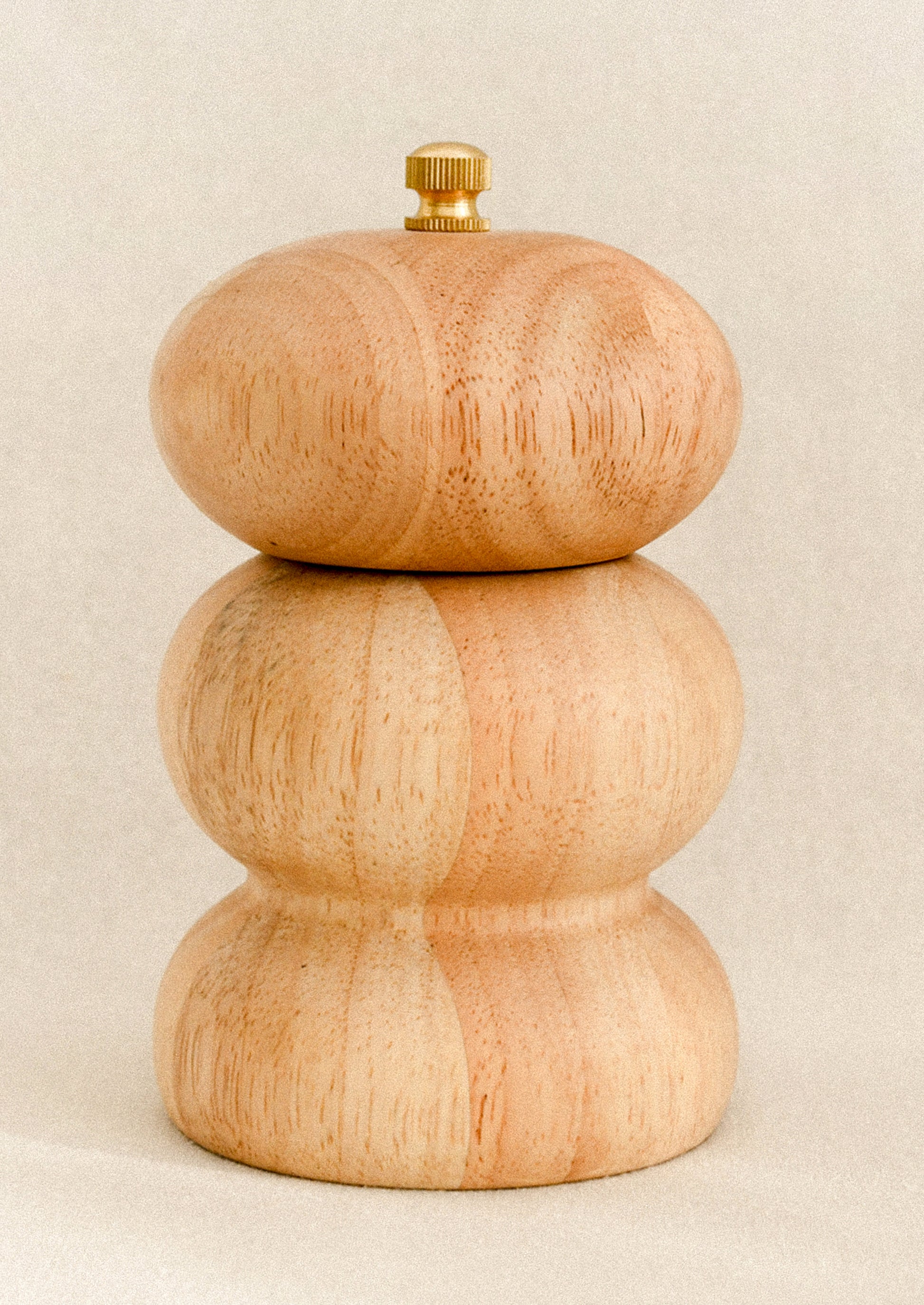 Wooden pepper grinder with a gold top on a beige background