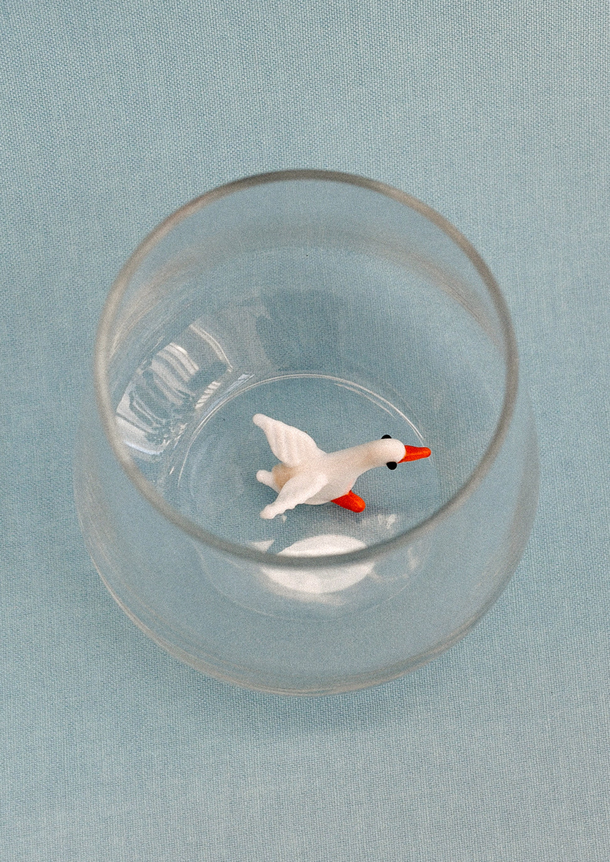 Clear glass tumbler with a small duck figure on a light blue background