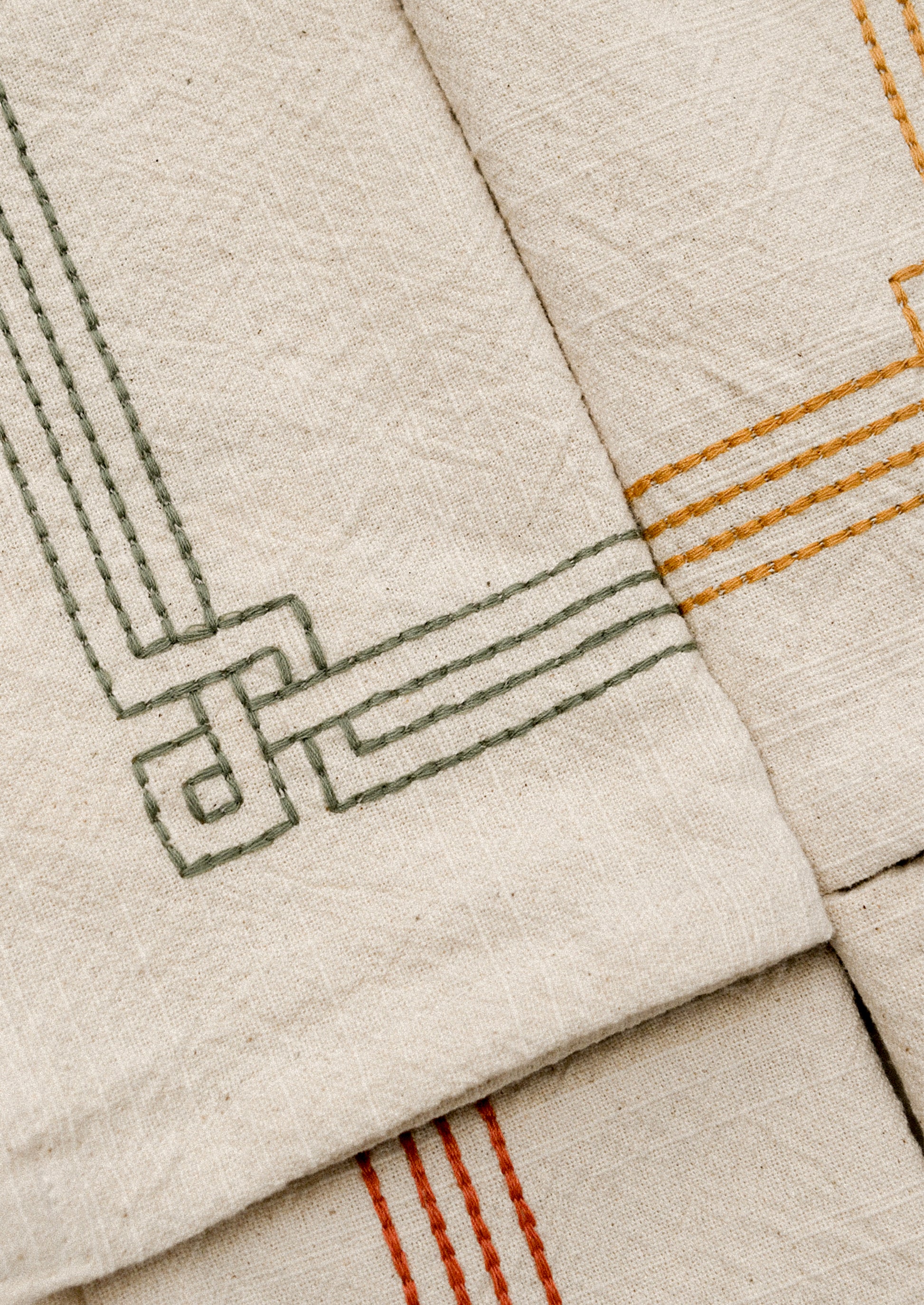 Set of beige napkins with embroidered geometric patterns in various colors on a white surface.