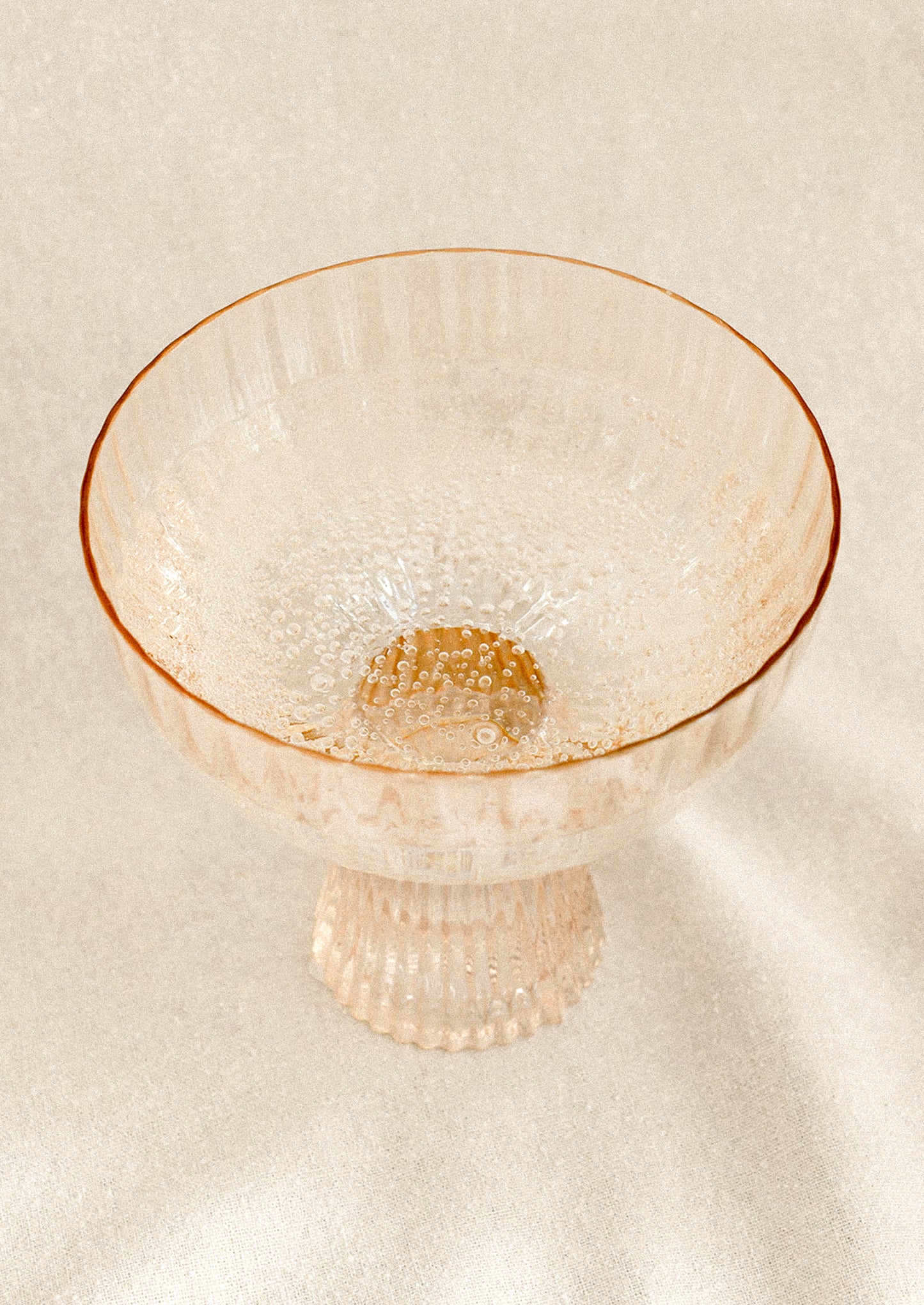 A coupe glass with fluted texture in peach color with iridescent finish.