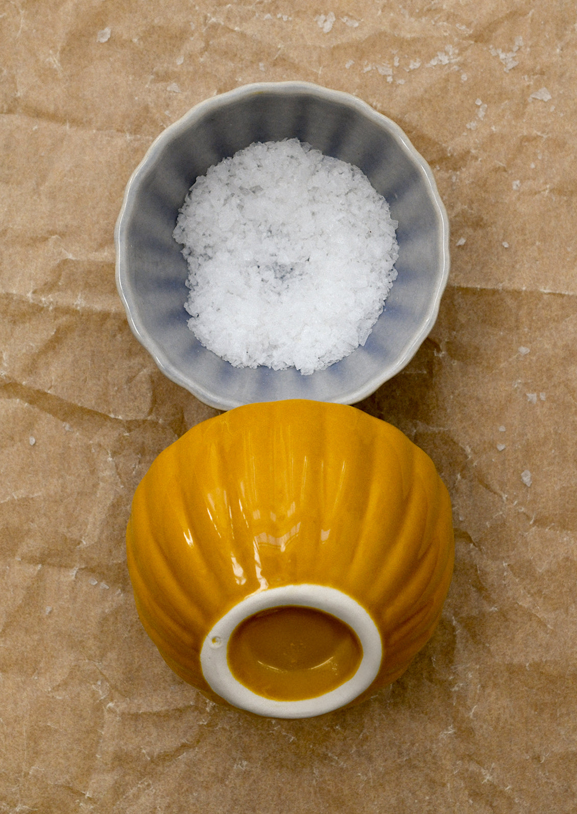 Small gray bowl with salt and yellow bowl on brown paper.