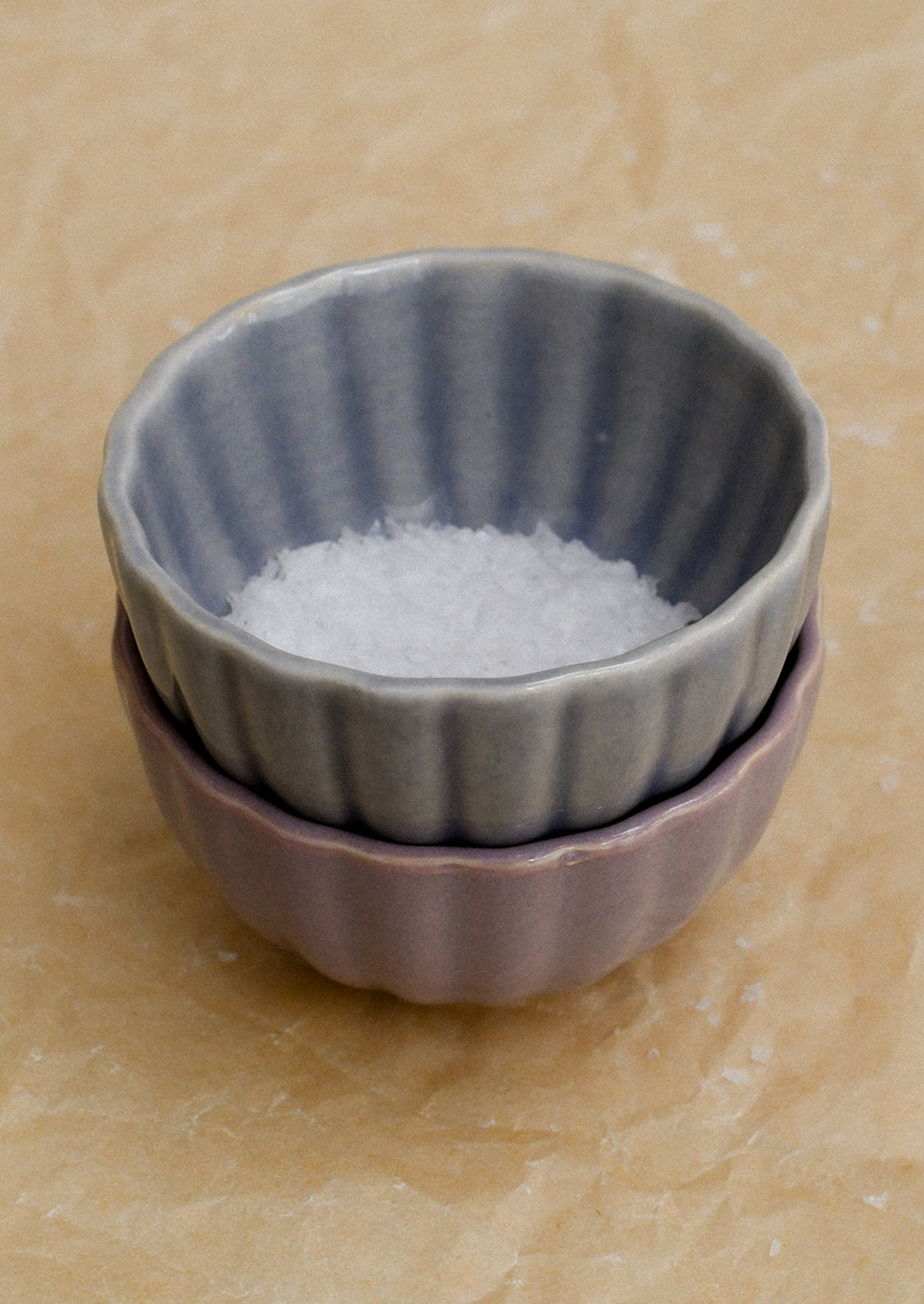 Two stacked ceramic bowls with salt on a beige surface