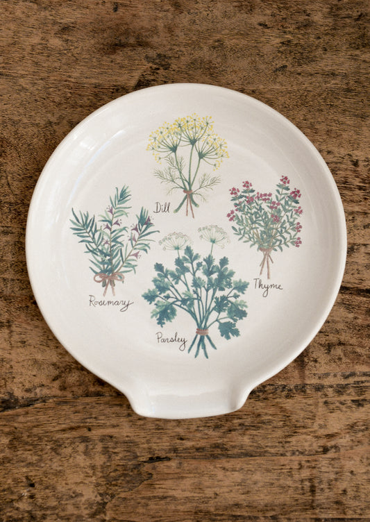 Decorative spoon rest with herb illustrations on a wooden surface
