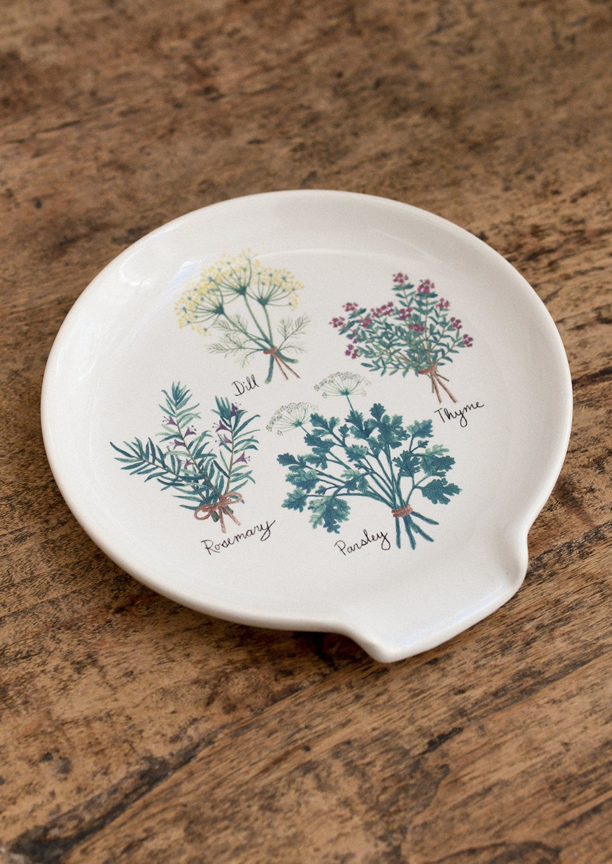 Decorative spoon rest with herb illustrations on a wooden surface