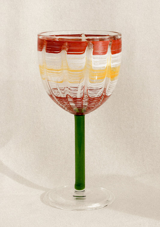 A wine glass with green stem and hand painted cup with abstract line pattern.