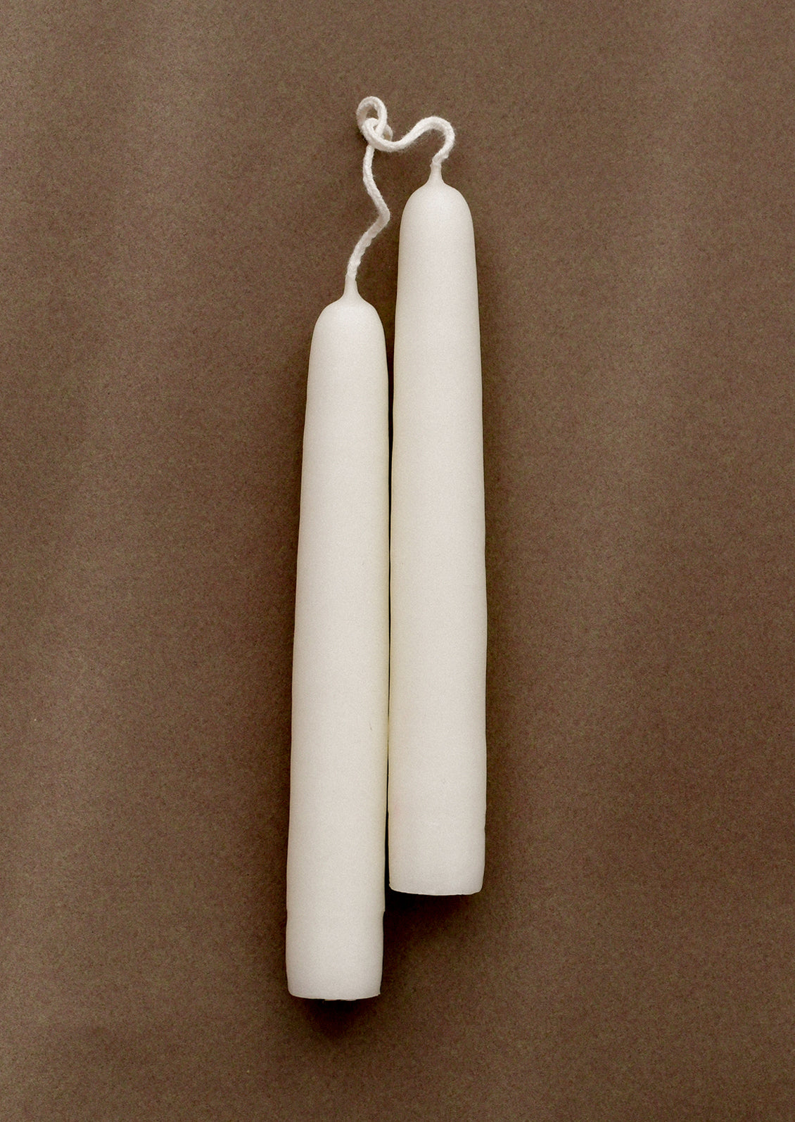 A pair of short white taper candles on a brown background.
