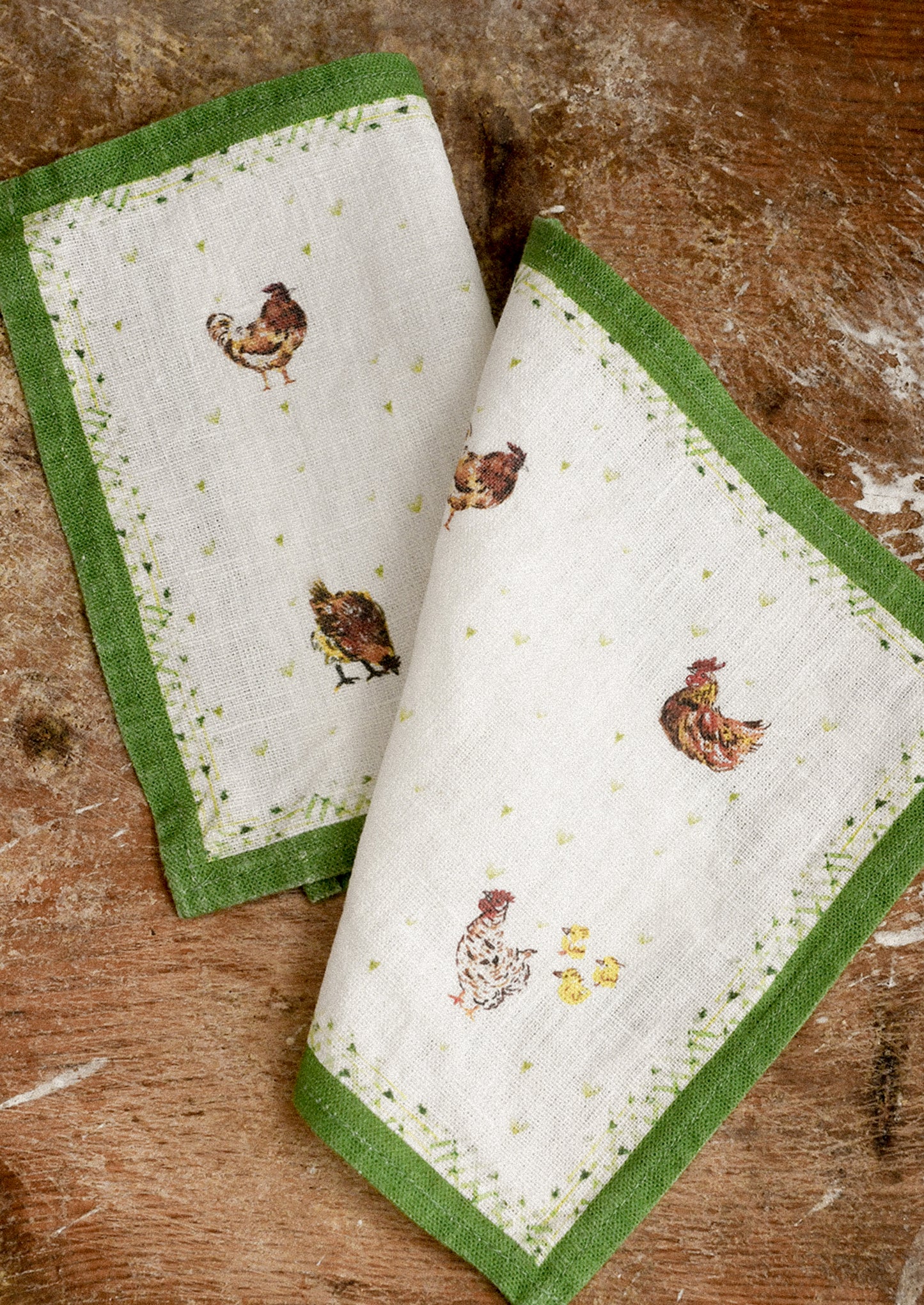 Set of four cocktail napkins with green borders and chicken designs on a wooden surface