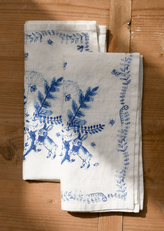 White napkins with blue floral and rabbit designs on a wooden surface