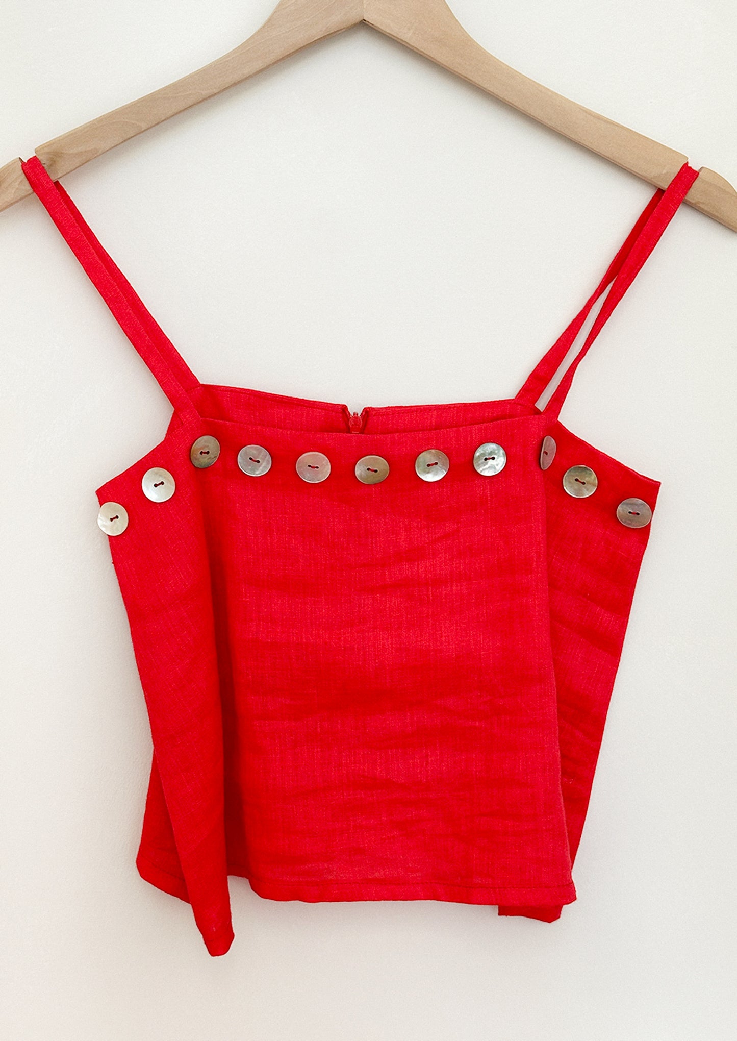 Red crop top with button details on a wooden hanger against a white background