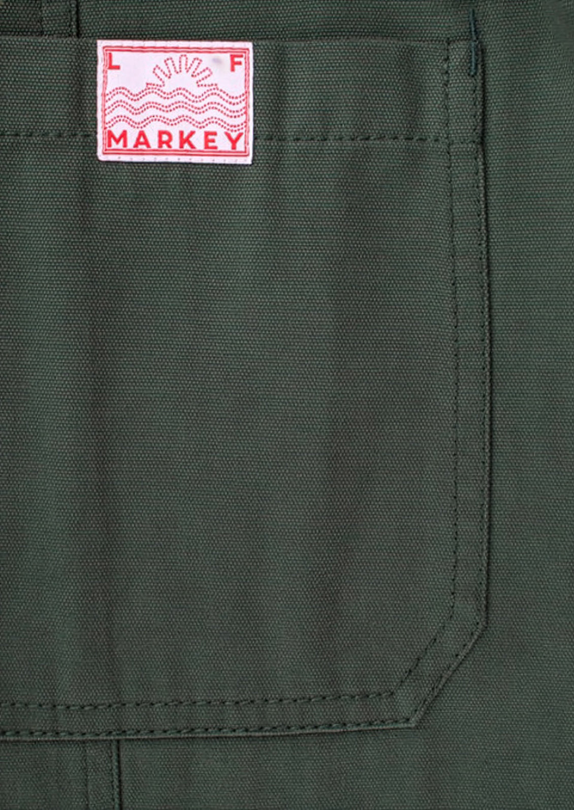 Close-up of a dark olive green canvas pocket with a white and red Markey brand patch on the upper left.