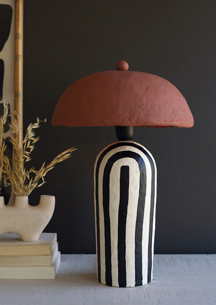 A table lamp with black and white striped base, terracotta shade.