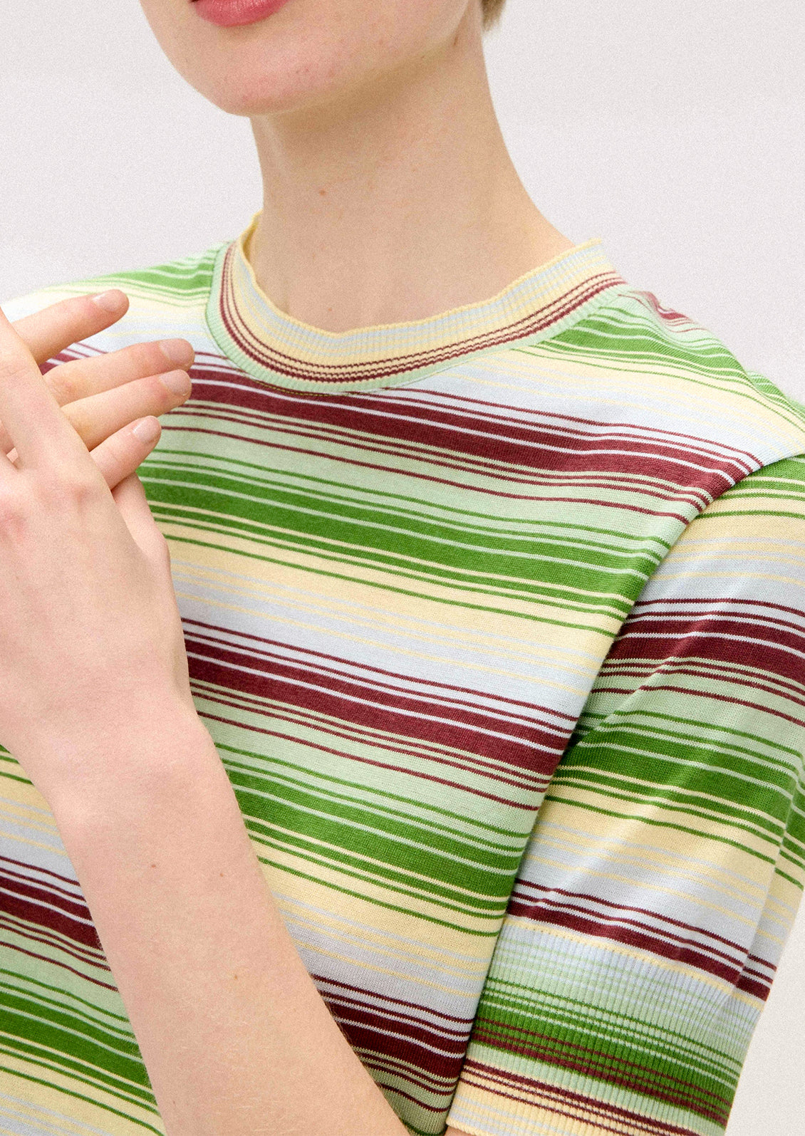 A person wearing a knit t-shirt with multi stripe pattern in green, cream and brown.