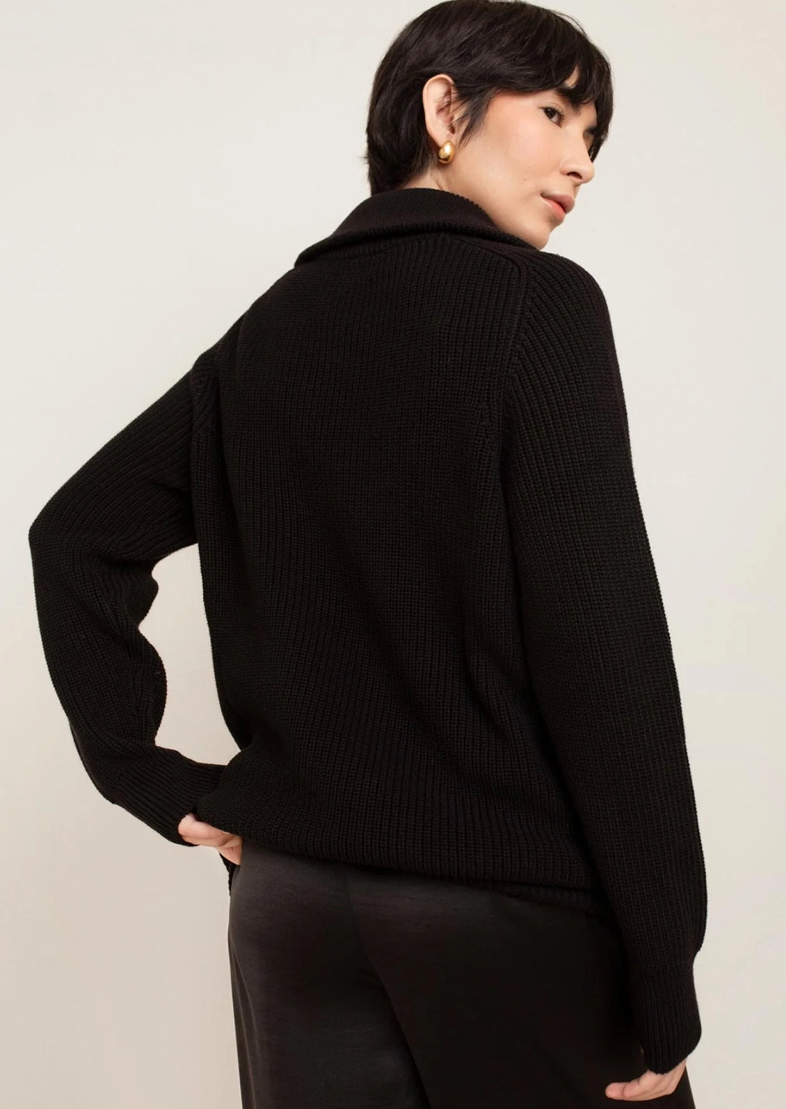 A person wearing a black sweater with silver zip at funnel neck.