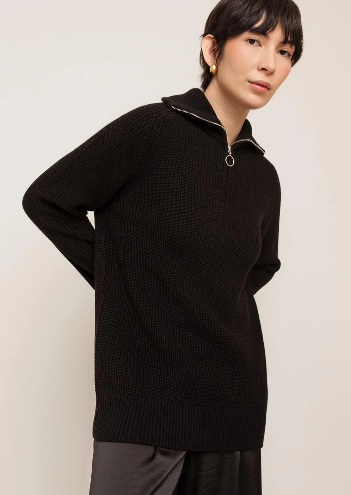 A person wearing a black sweater with silver zip at funnel neck.