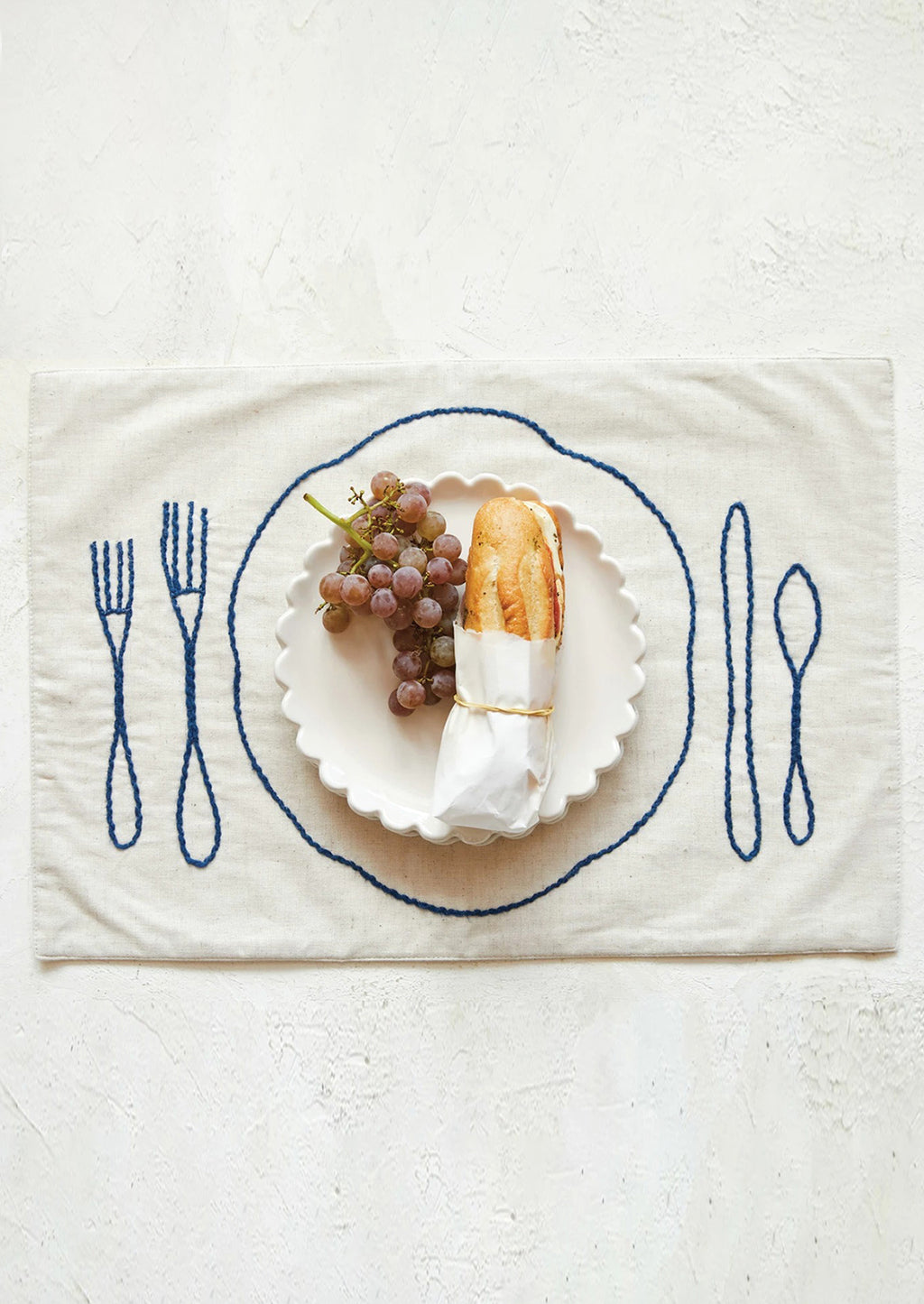 1: An off-white linen-cotton placemat with navy blue plate and silverware embroidery.