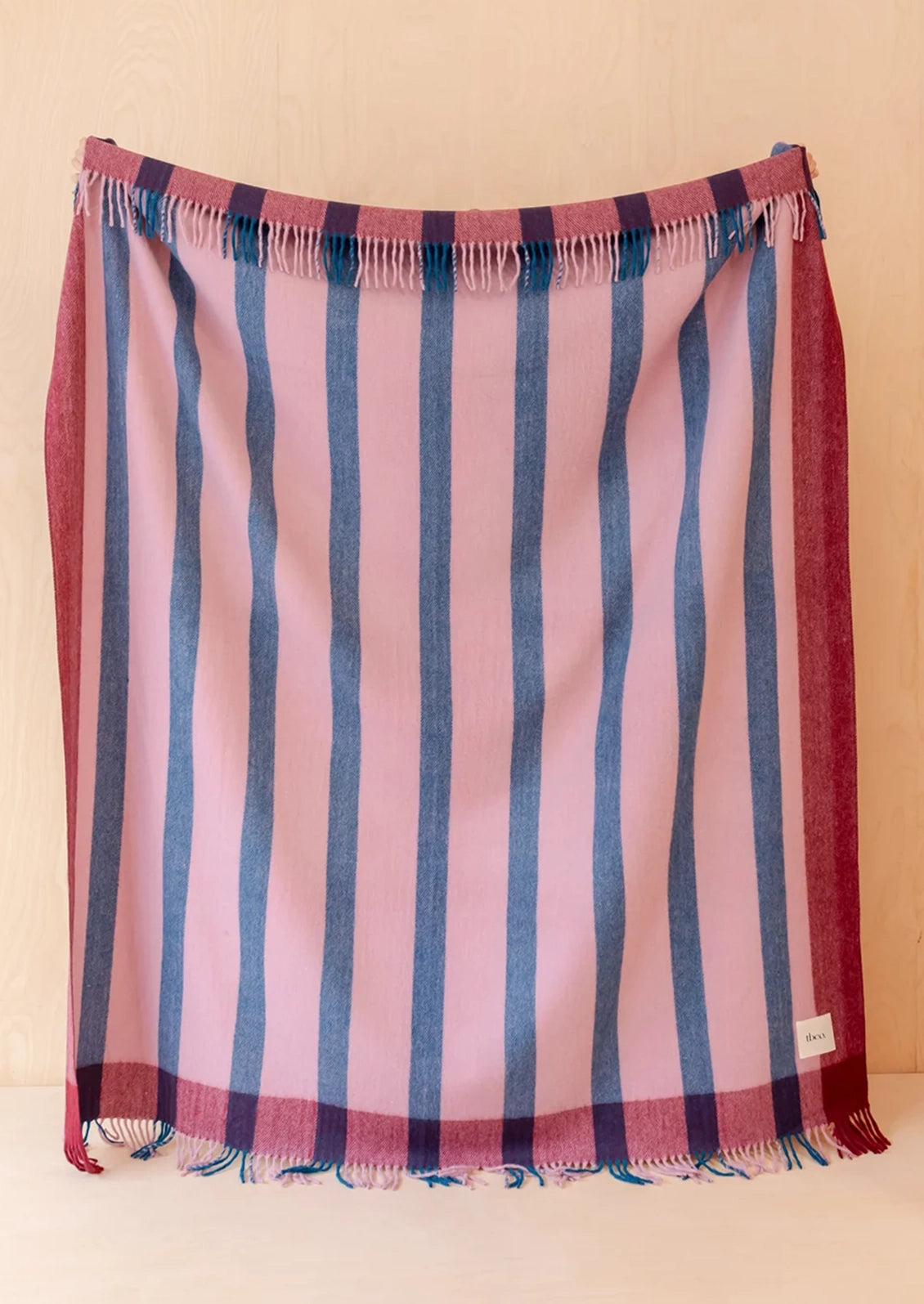 A throw blanket with vertical pink and blue stripes, fringed along the top and bottom edges.