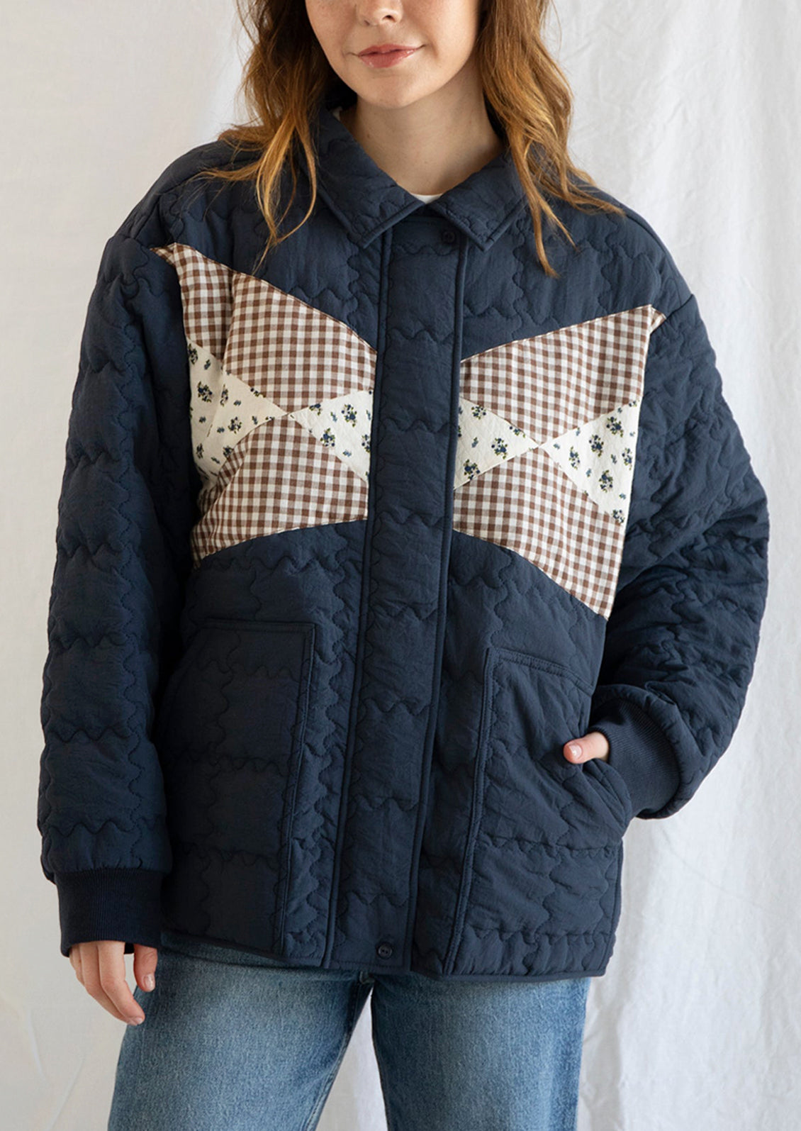 A woman wearing a navy blue jacket with squiggle shaped quilting and gingham and floral patchwork detailing at front.