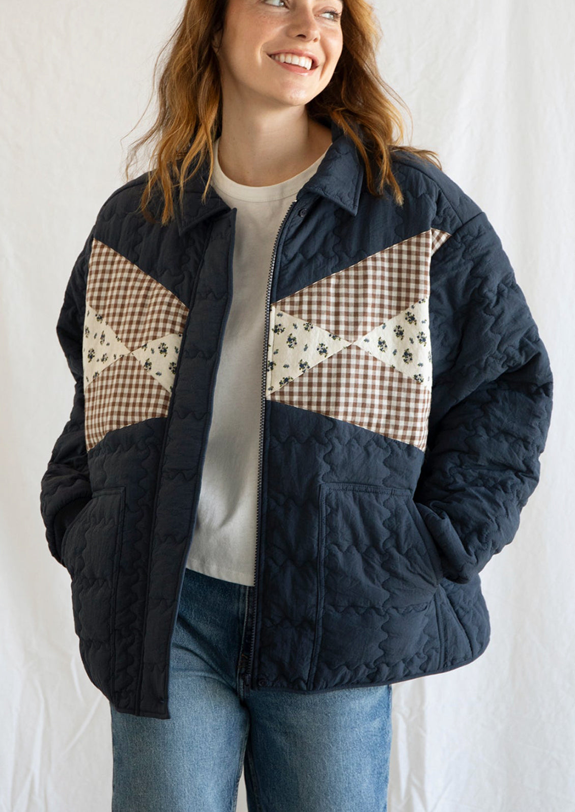 A woman wearing a navy blue jacket with squiggle shaped quilting and gingham and floral patchwork detailing at front.